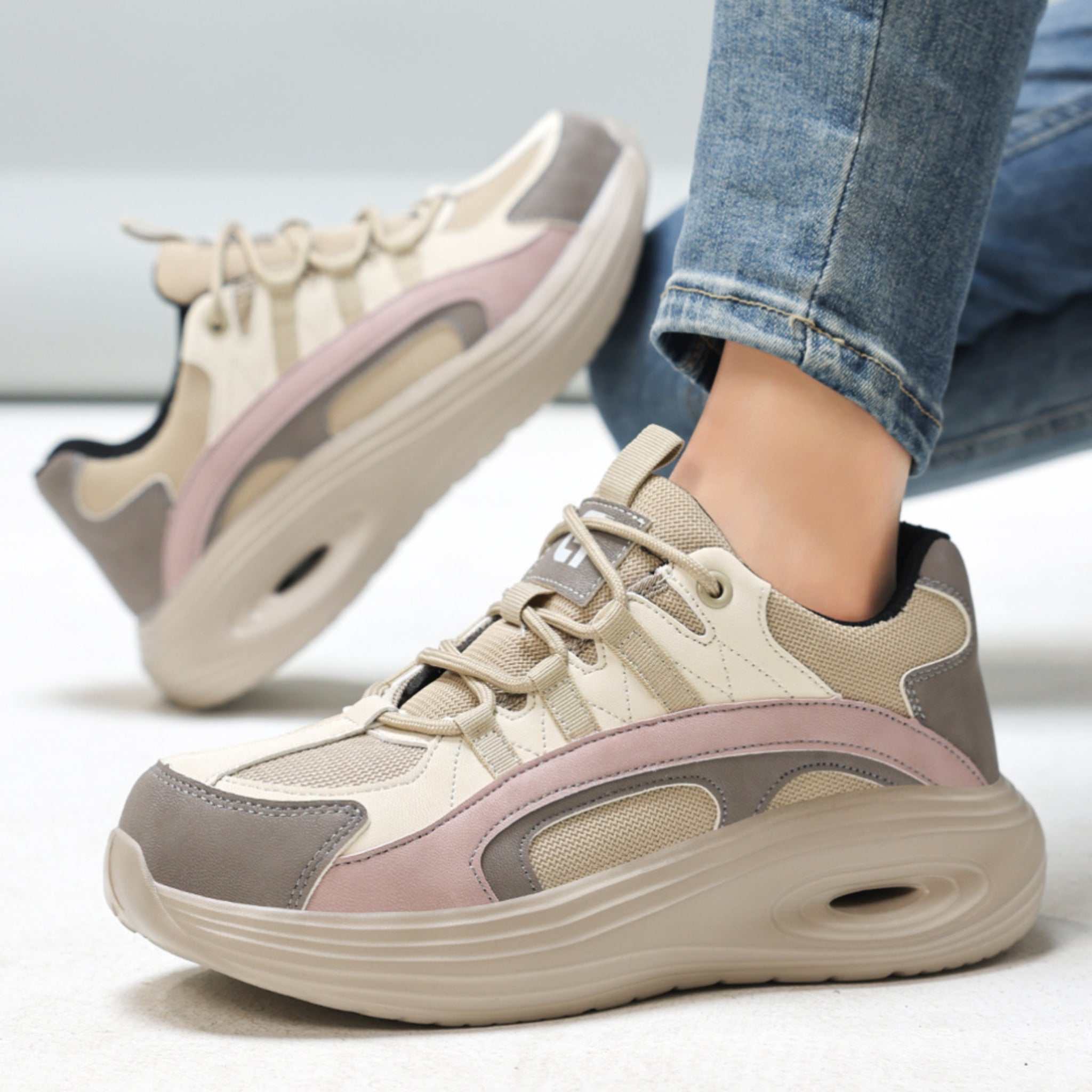 A close-up photograph of SafeStep women's safety sneakers, focusing on the pink and grey leather-mesh patchwork upper, classic lacing system, and branded tongue for a fashionable workwear style.