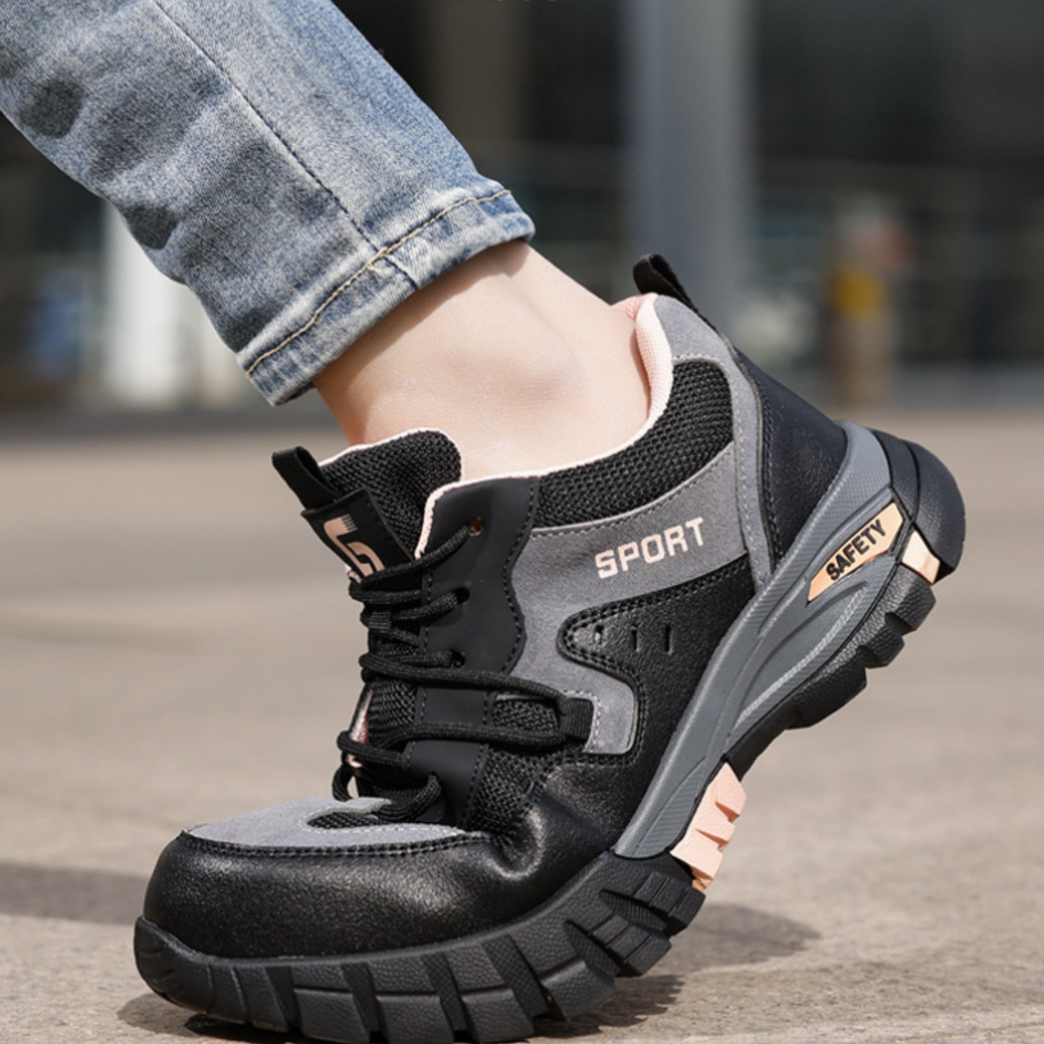 A lifestyle on-foot view of SafeStep Lady safety sneakers in black and pink, styled with denim jeans, showcasing the reinforced heel support and anti-slip rubber outsole.